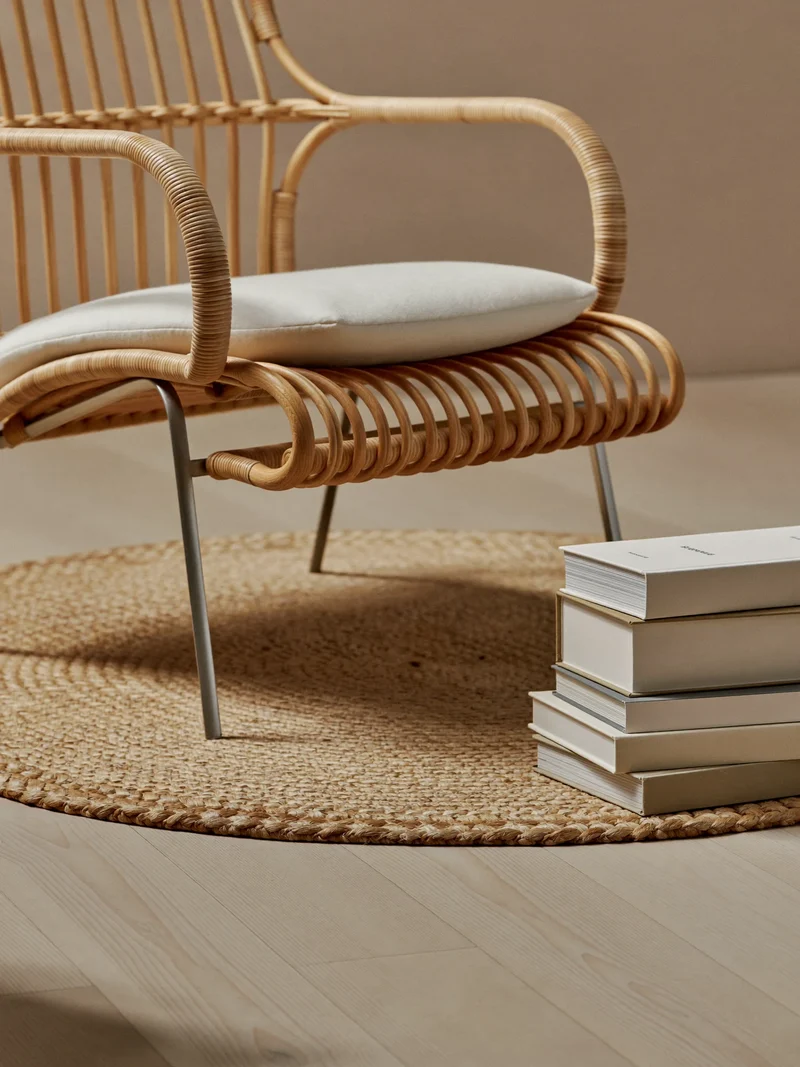 Illustration: runder Jute-Baumwoll-Teppich unter Rattansessel in einer Leseecke